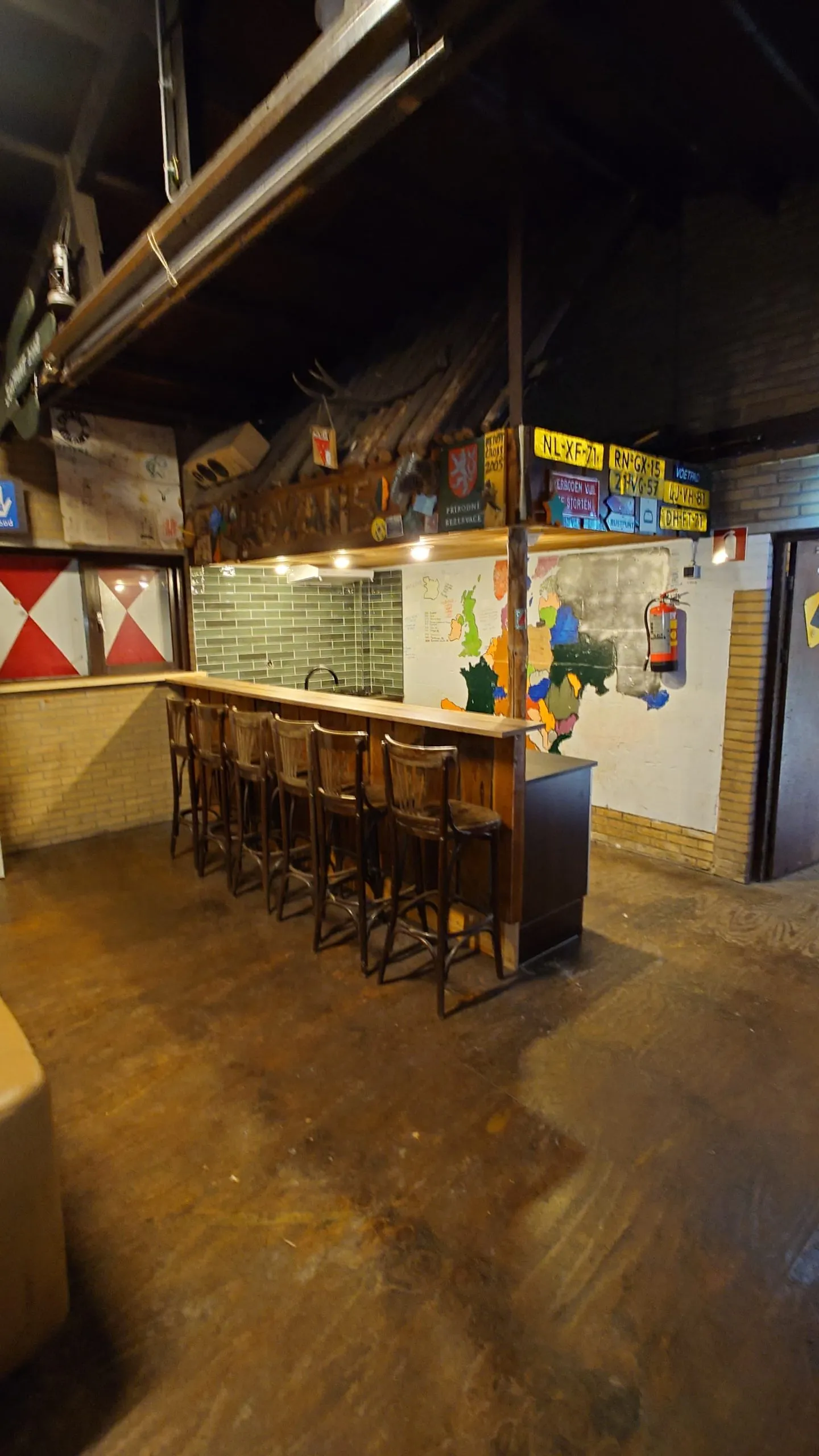 Houten bar met een rij barkrukken en borden aan de wand