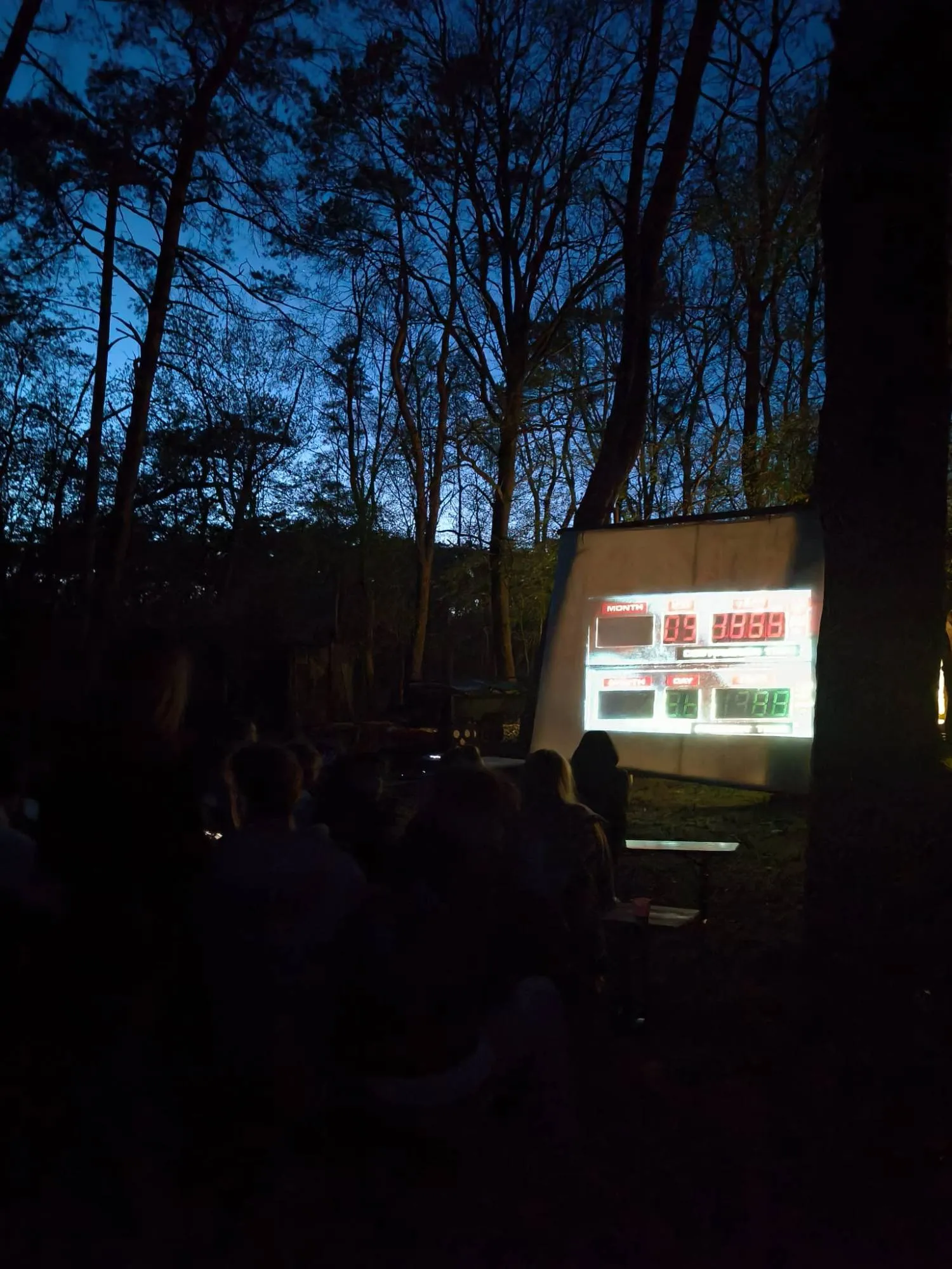 Scouts kijken 's avonds in het bos naar een film op een groot scherm
