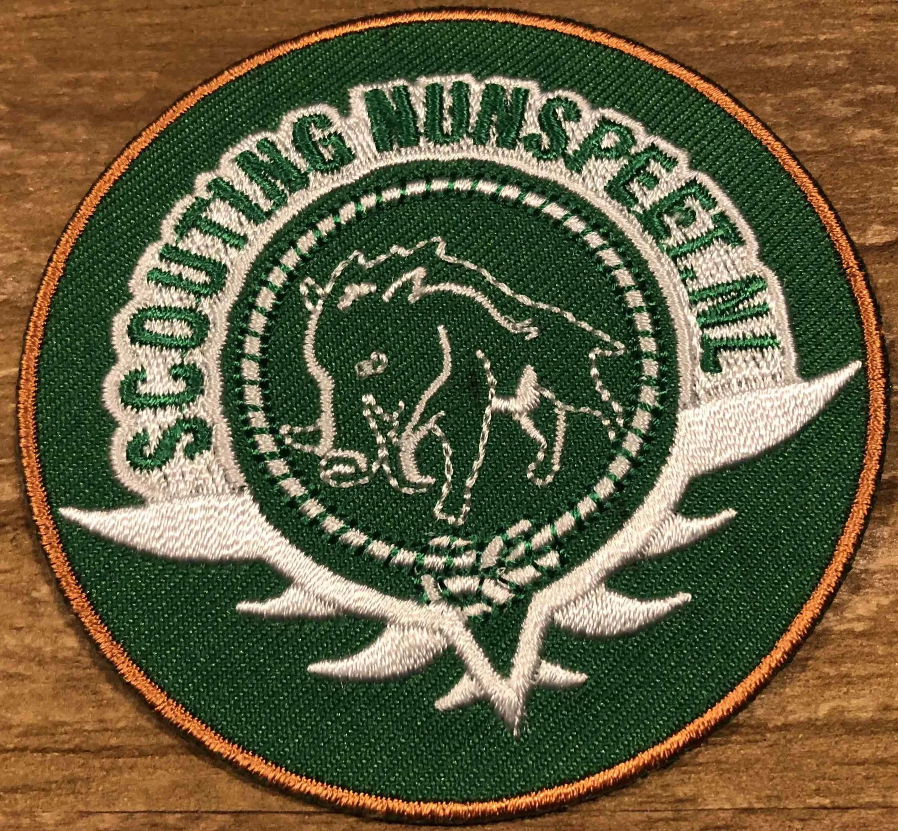 Groen geborduurd embleem van Scouting Nunspeet met een everzwijn in het midden