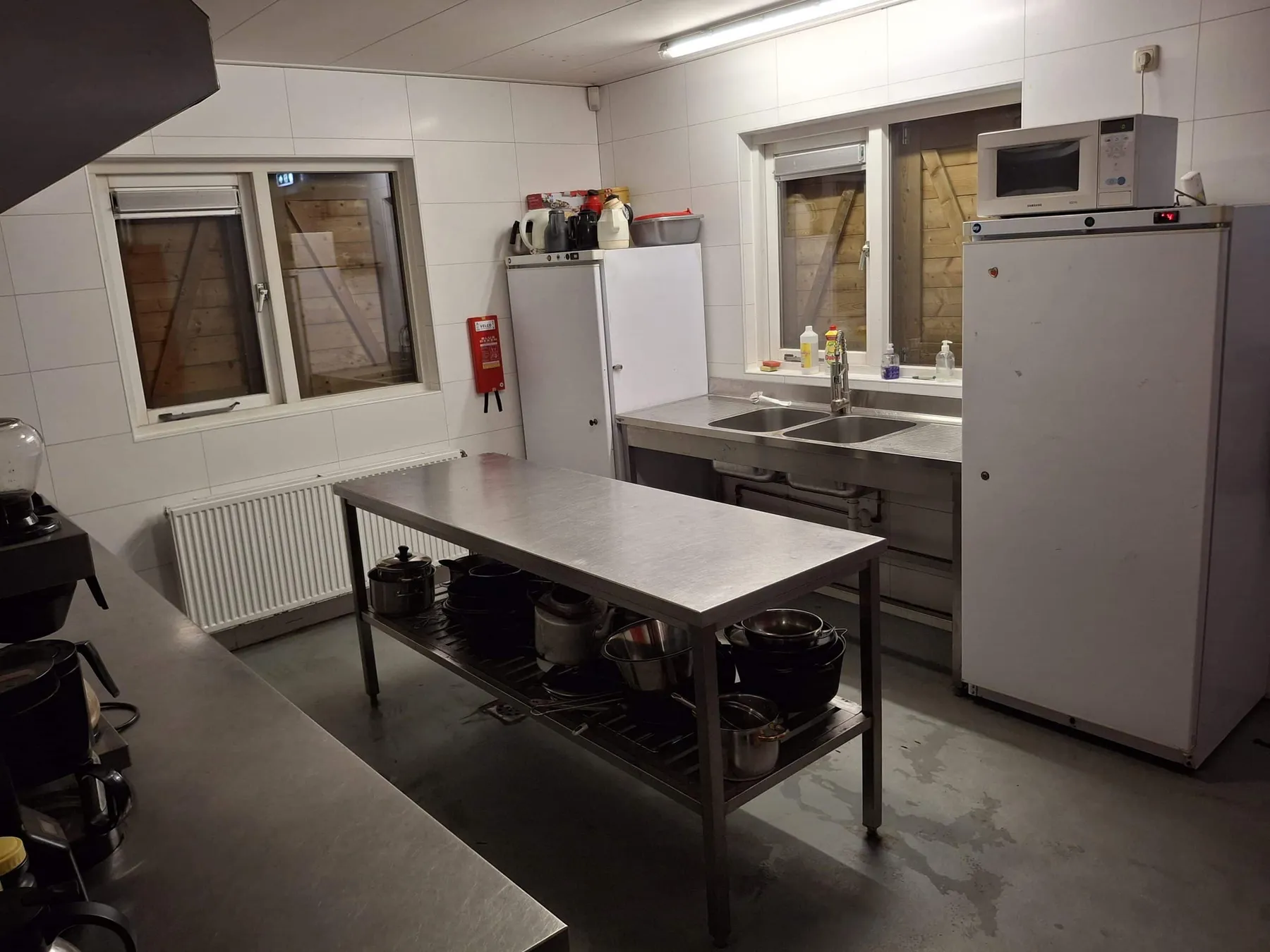 Keuken met RVS werktafel vol pannen, spoelbak, koelkast en magnetron