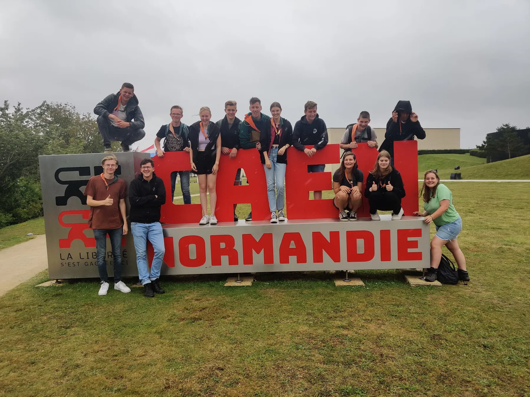 Explorers zitten en staan op grote rode letters van Caen Normandie