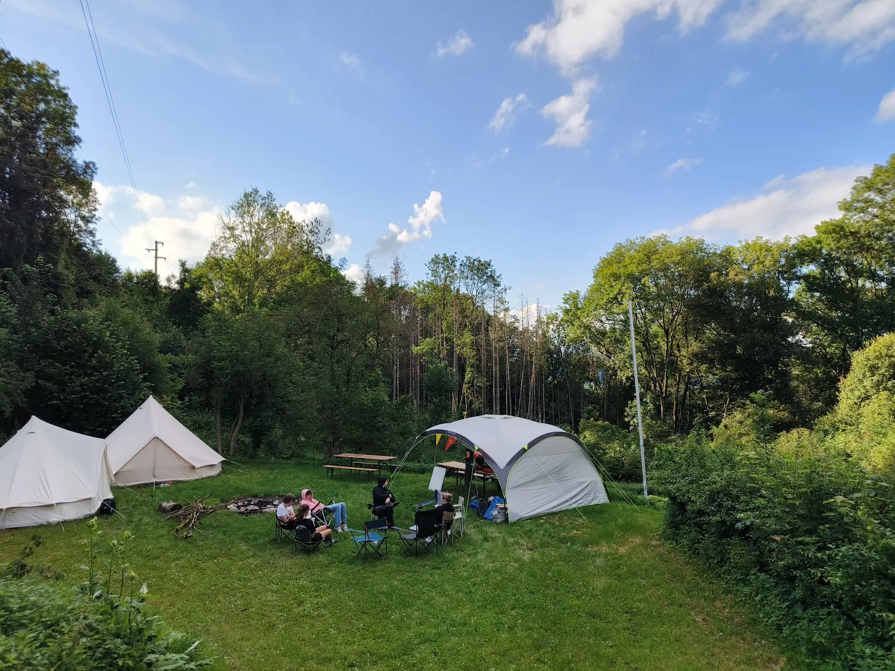 Tenten en een partytent op een grasveld tussen de bomen tijdens het zomerkamp